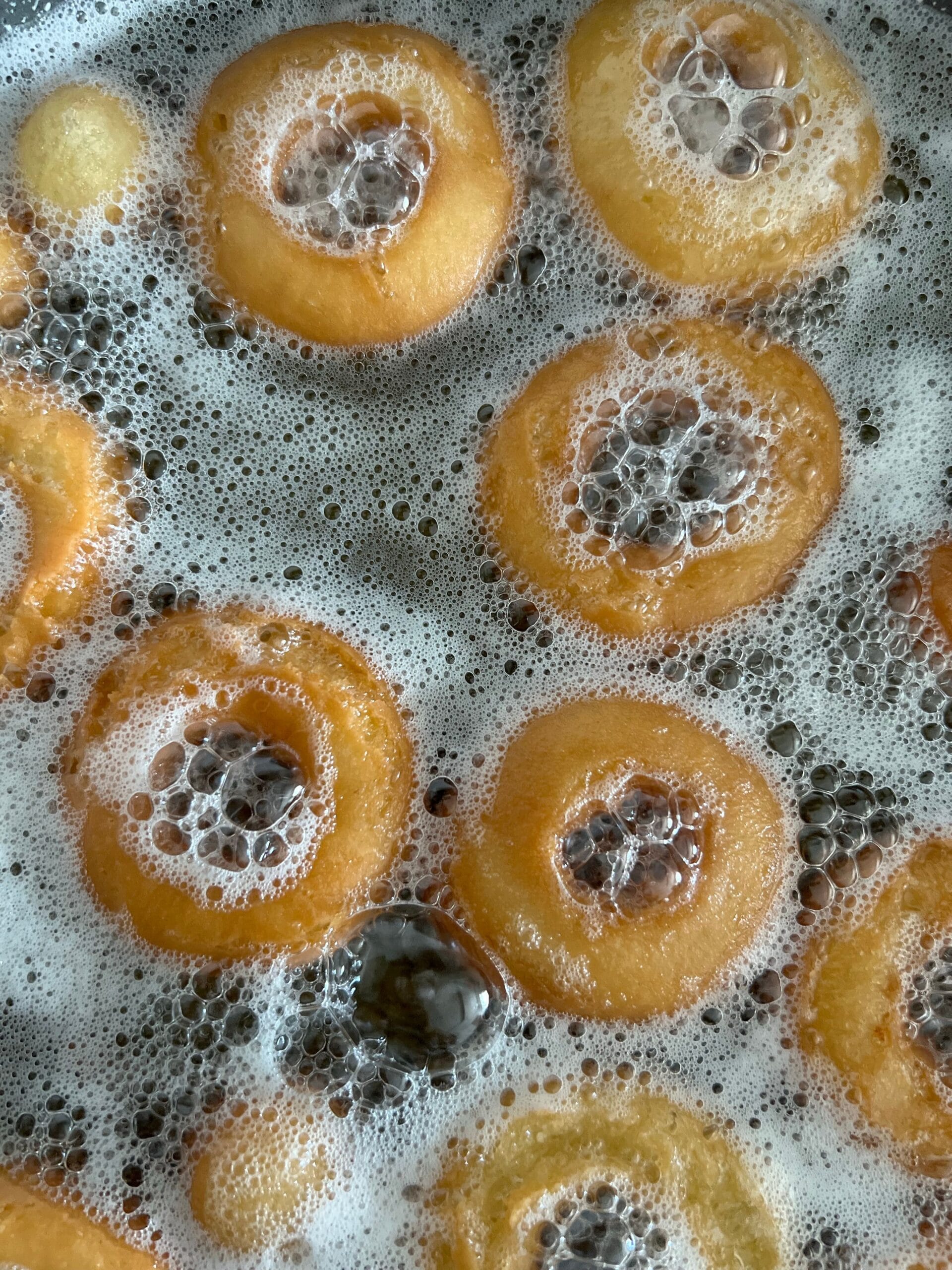 Golden donuts frying in hot oil, developing a deep-fried crust.