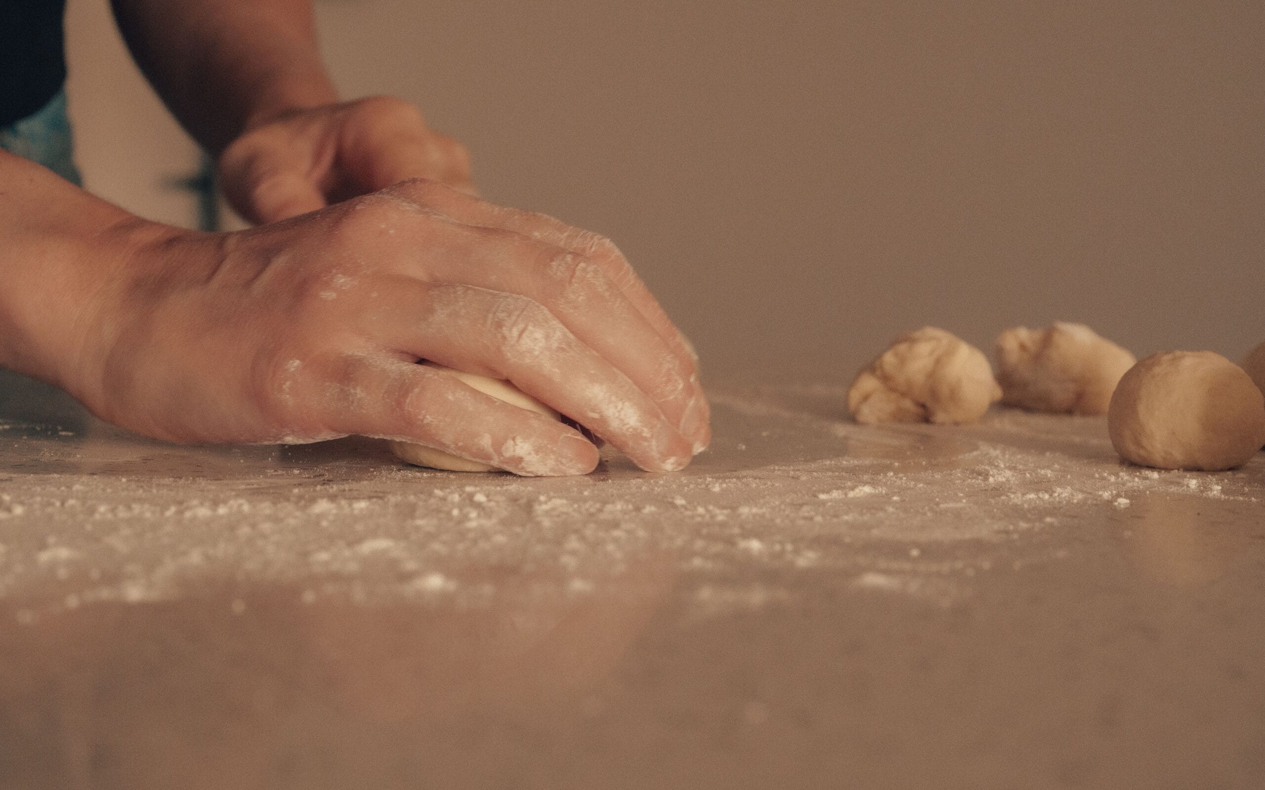 Hands kneading soft yeast dough on a lightly floured countertop before the first rise.